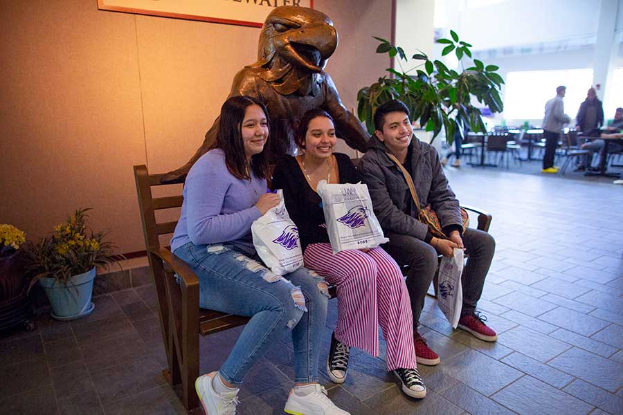 People sitting on a bench with a Willie Statue in the University Center.