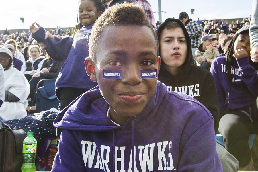 A young person wears a purple Warhawks sweathshirt and smiles at the camera.