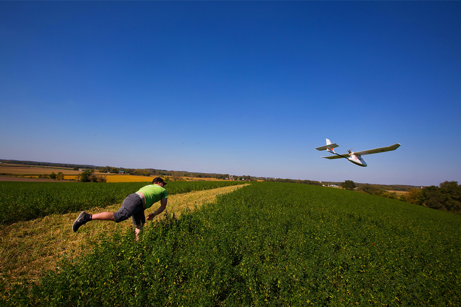 A student throws a GIS drone into the air in a field.