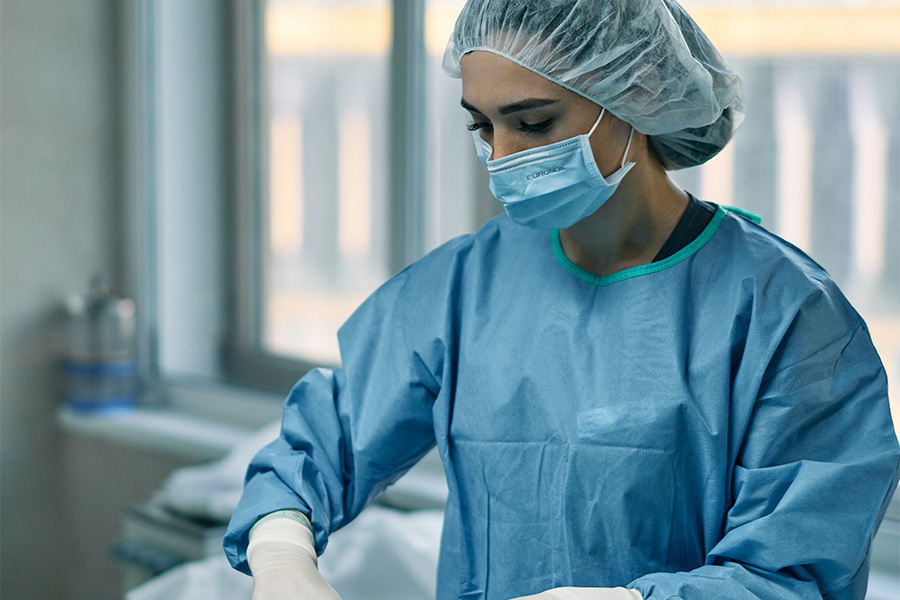 A person wears scrubs, a hair net and a mask over their face.