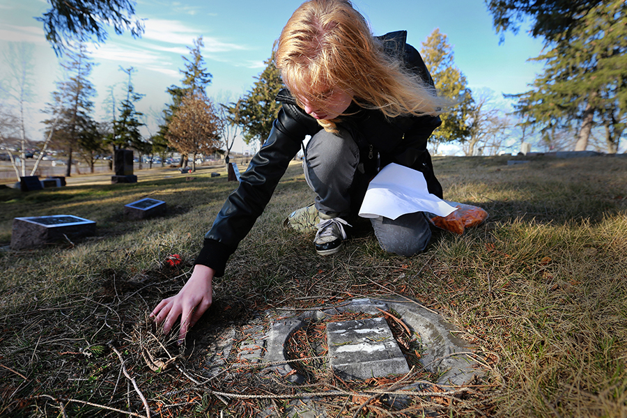 A student brushes away debris covering a grave marker.