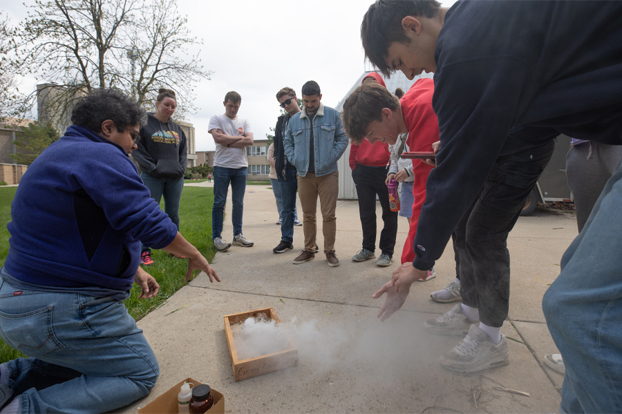 A faculty members demonstrates volcanic activity as smoke rises from a box.