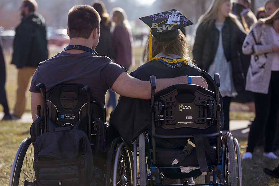 Two people in wheelchairs with their arms each other at graduation.