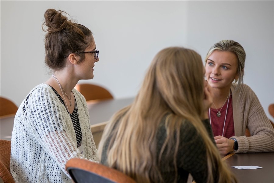 Three people talk as they sit together at a table.