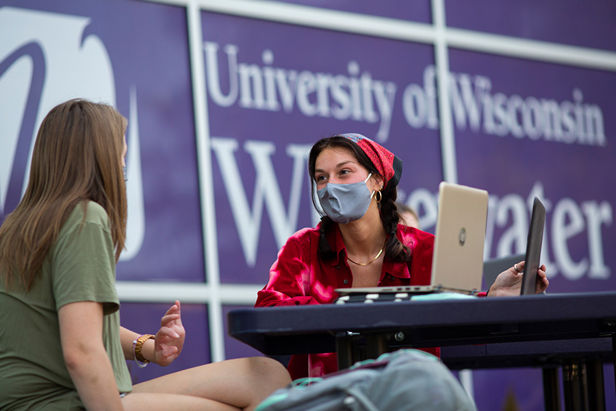 Two people sitting at a table with a UW-Whitewater banner behind them.