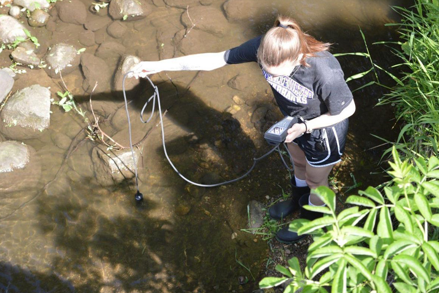 A person in a UW-Whitewater shirt works in a river.