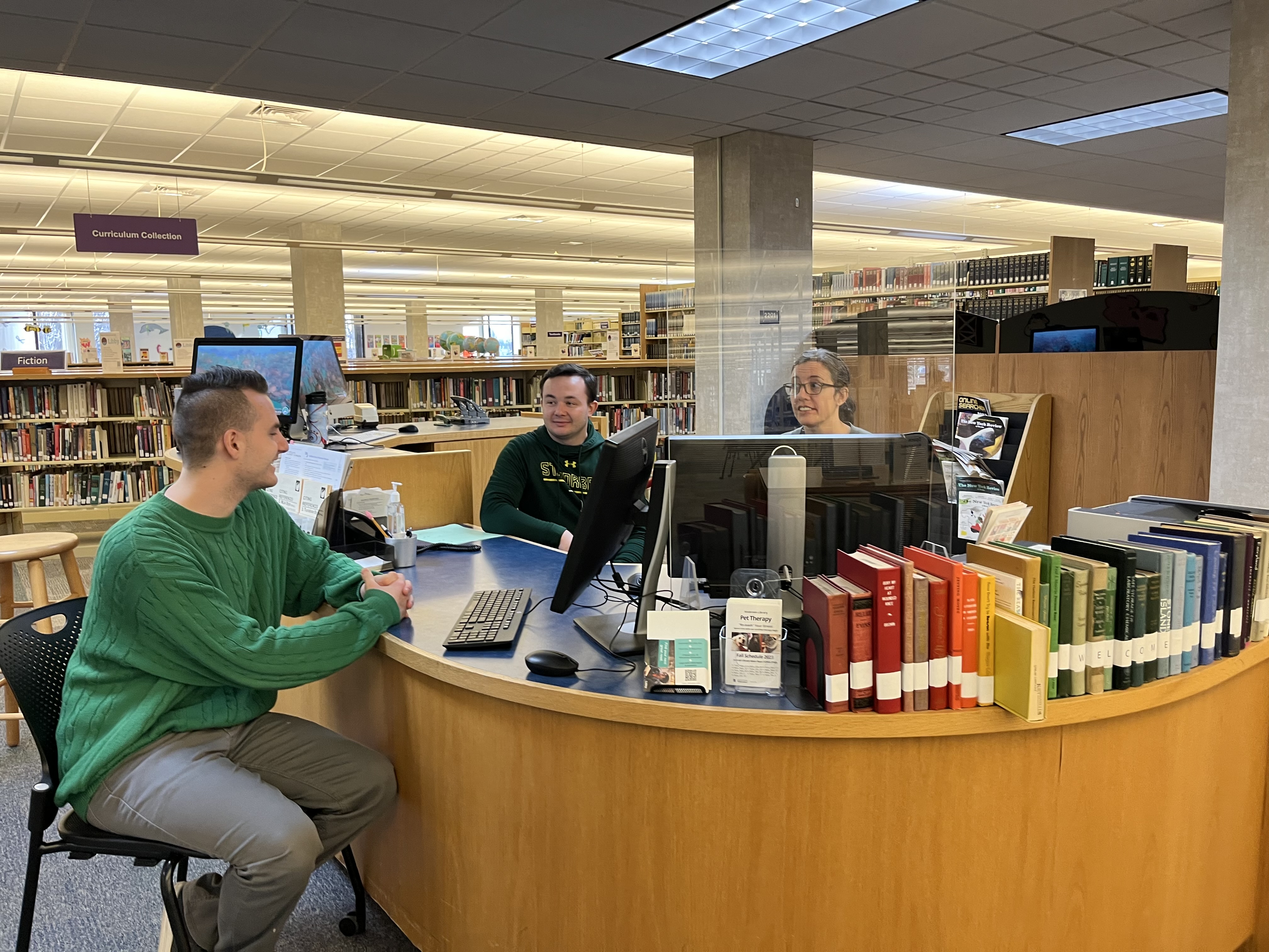 Student in green shirt getting help from the Andersen Library reference desk