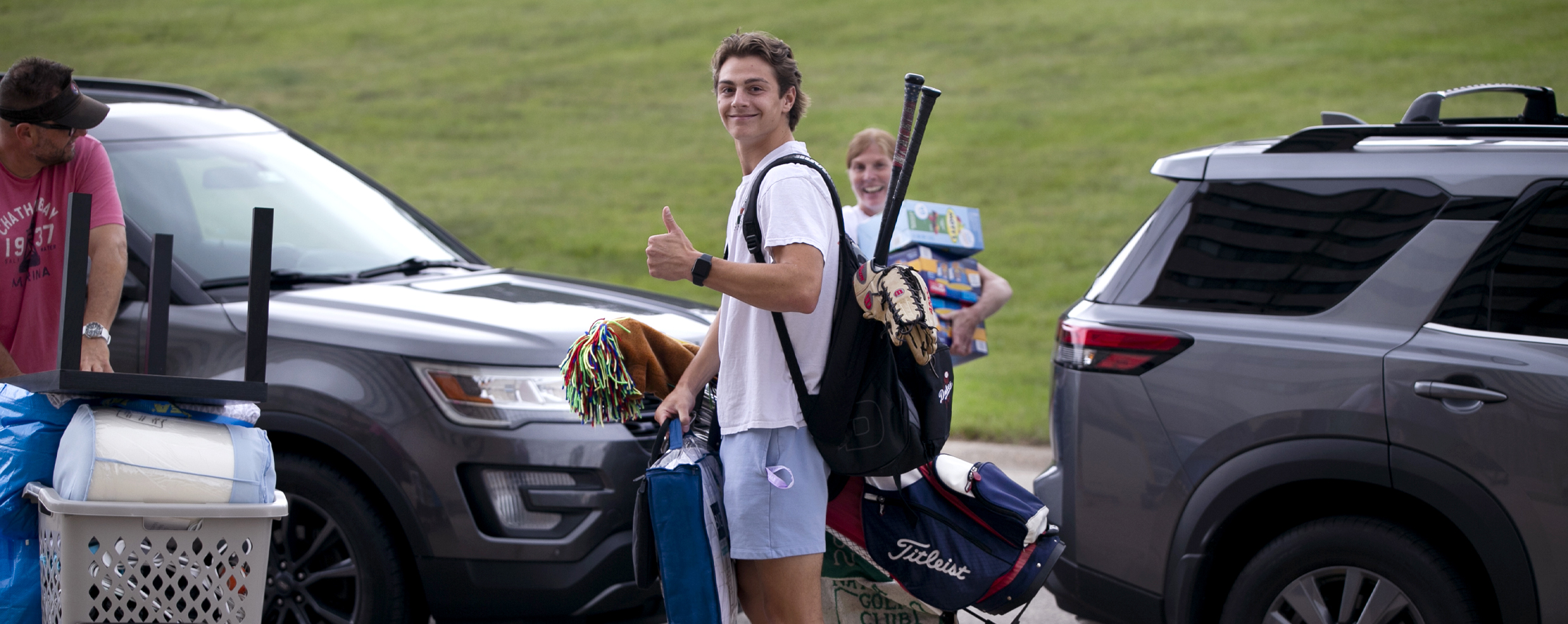 A student wearing a backpack with baseball bats sticking out gives thumbs up to the camera.