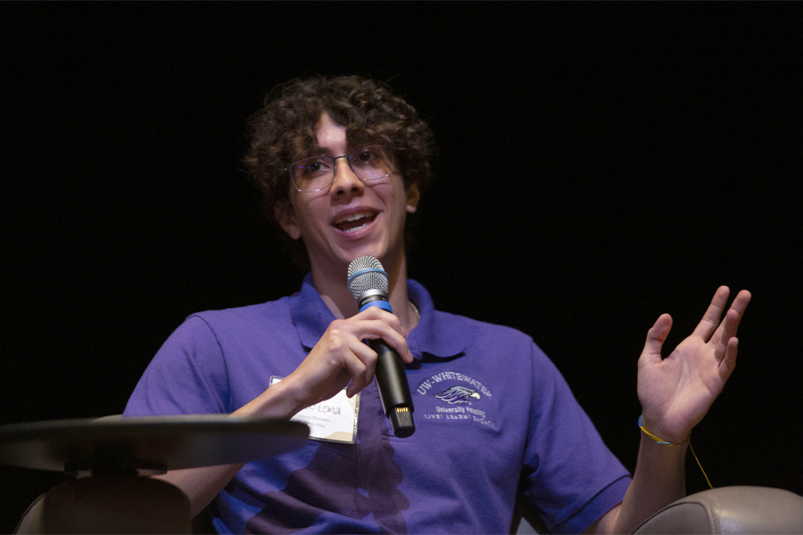 A young man in a purple shirt speaks into a microphone.