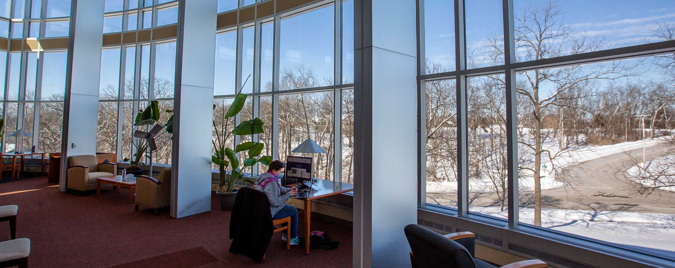 A student sits in front of the large windows in the Lenox Library on the UW-Whitewater Rock County campus.