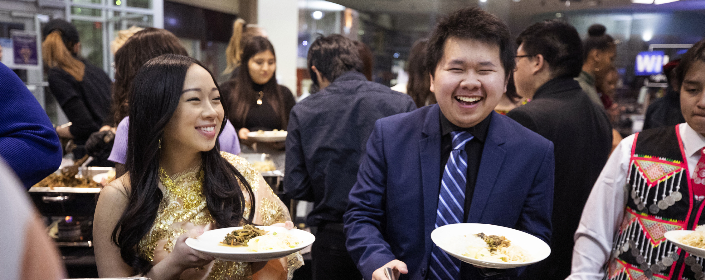 Two students smile with plates of food in their hands.