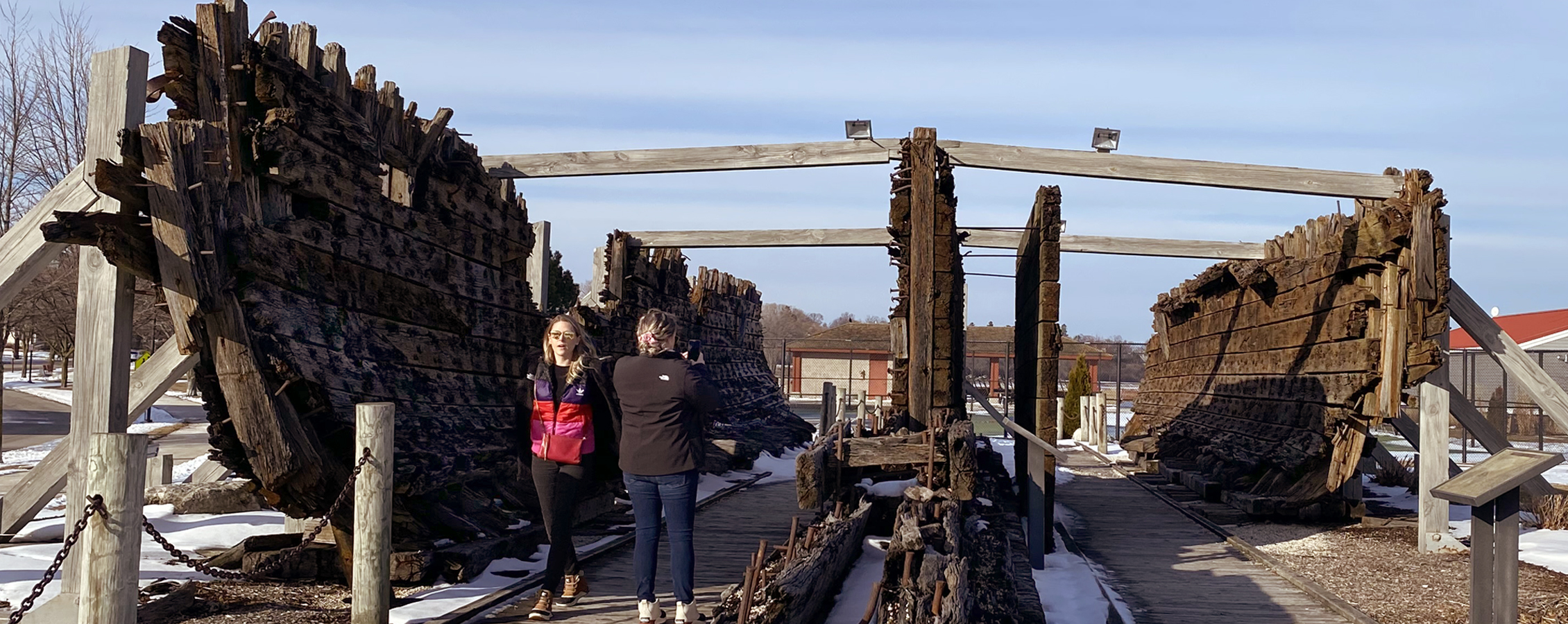 Students walk through remains of an old, large wooden boat.