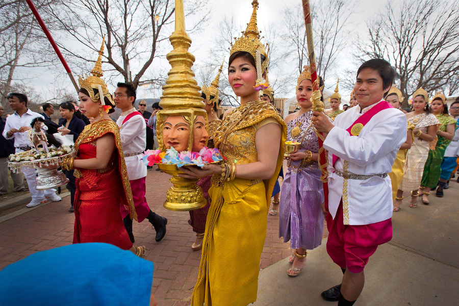 An Asian woman dressed in gold walks in a procession during a Khmer New Year celebration.