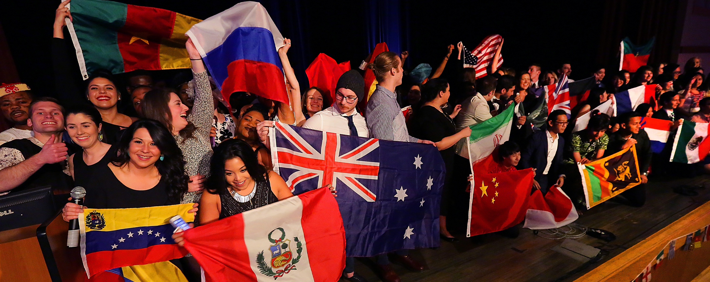 A large group of students hold flags from countries around the world.