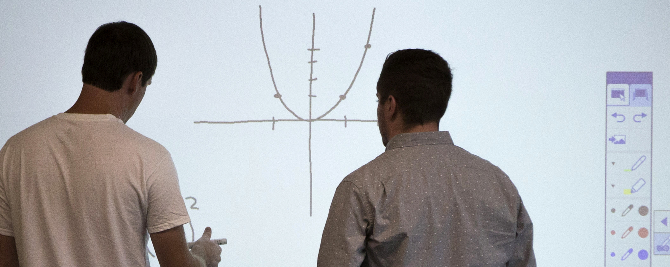 Two people work together at a white board, looking at a graph.