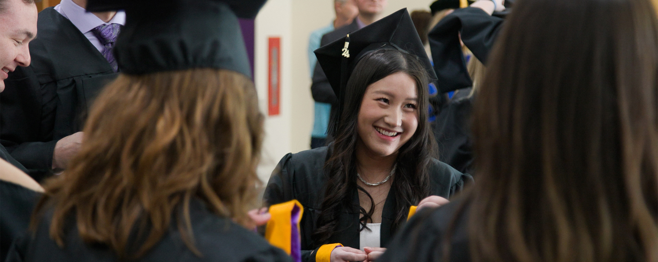 A school psychology student wearing cap and gown smiles while standing amongst other graduates.