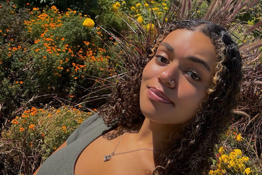 A person with long curly hair stands among yellow flowers.