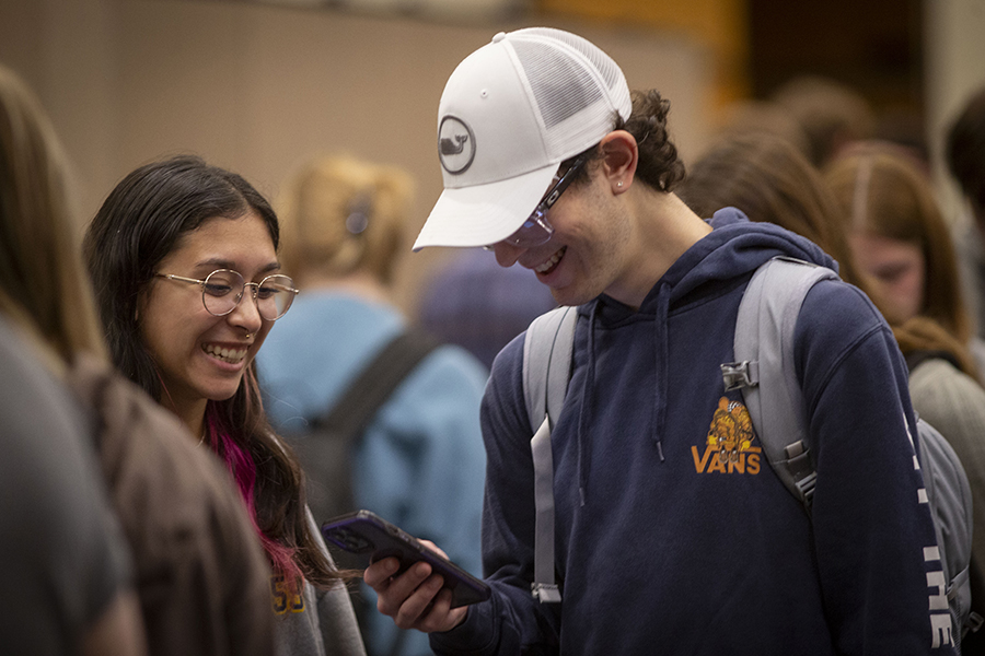 Two students smile together as they look at a phone.