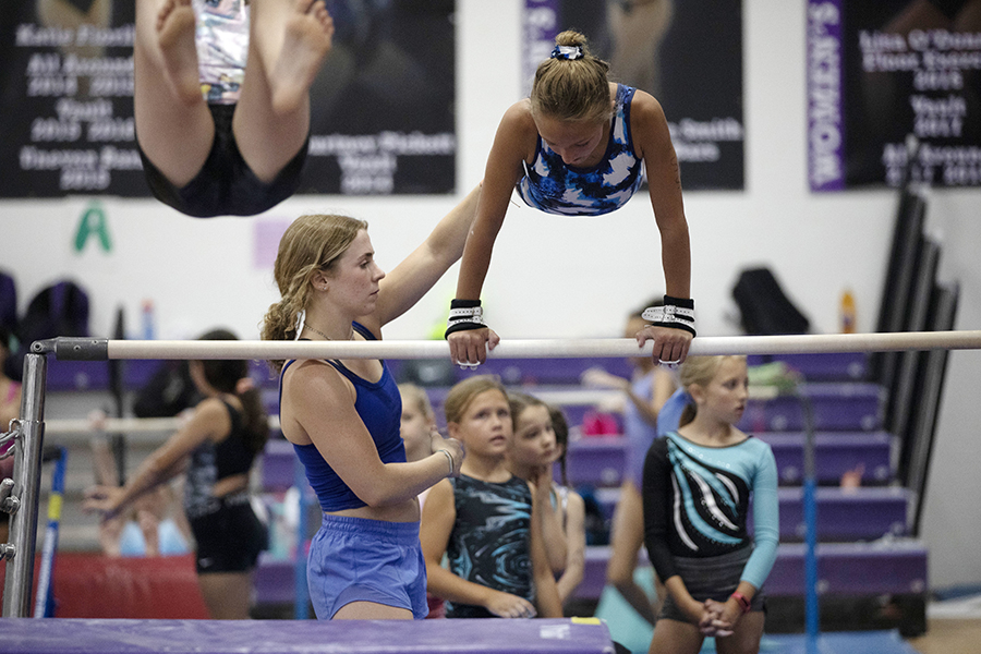 A person helps another person over a gymnastic bar.
