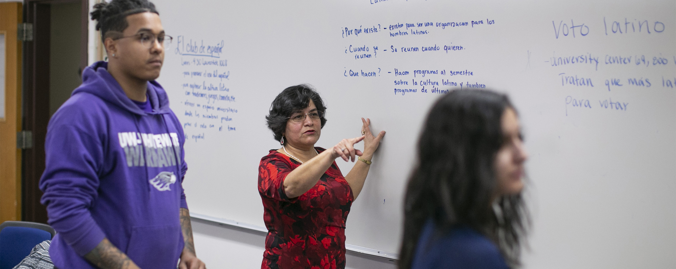 A Spanish faculty member directs students at a whiteboard.