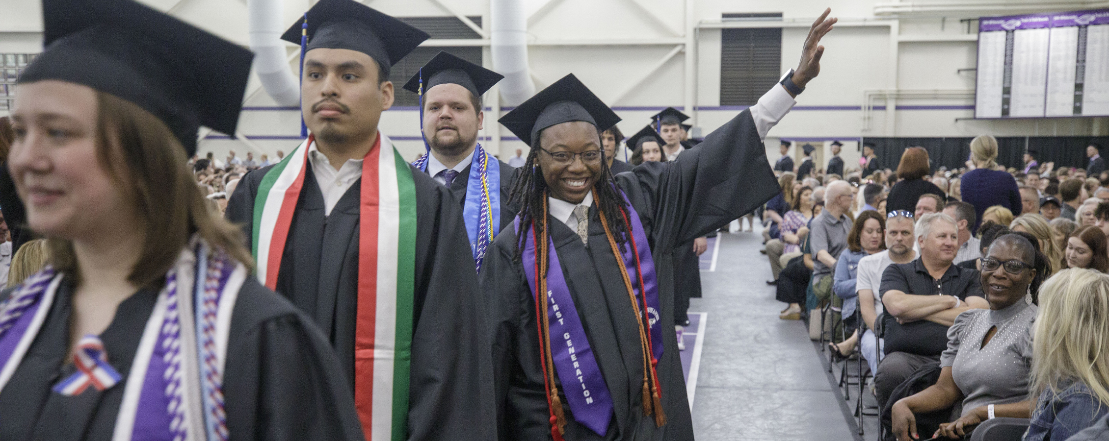 A student wearing academic regalia waves during the graduation ceremony.