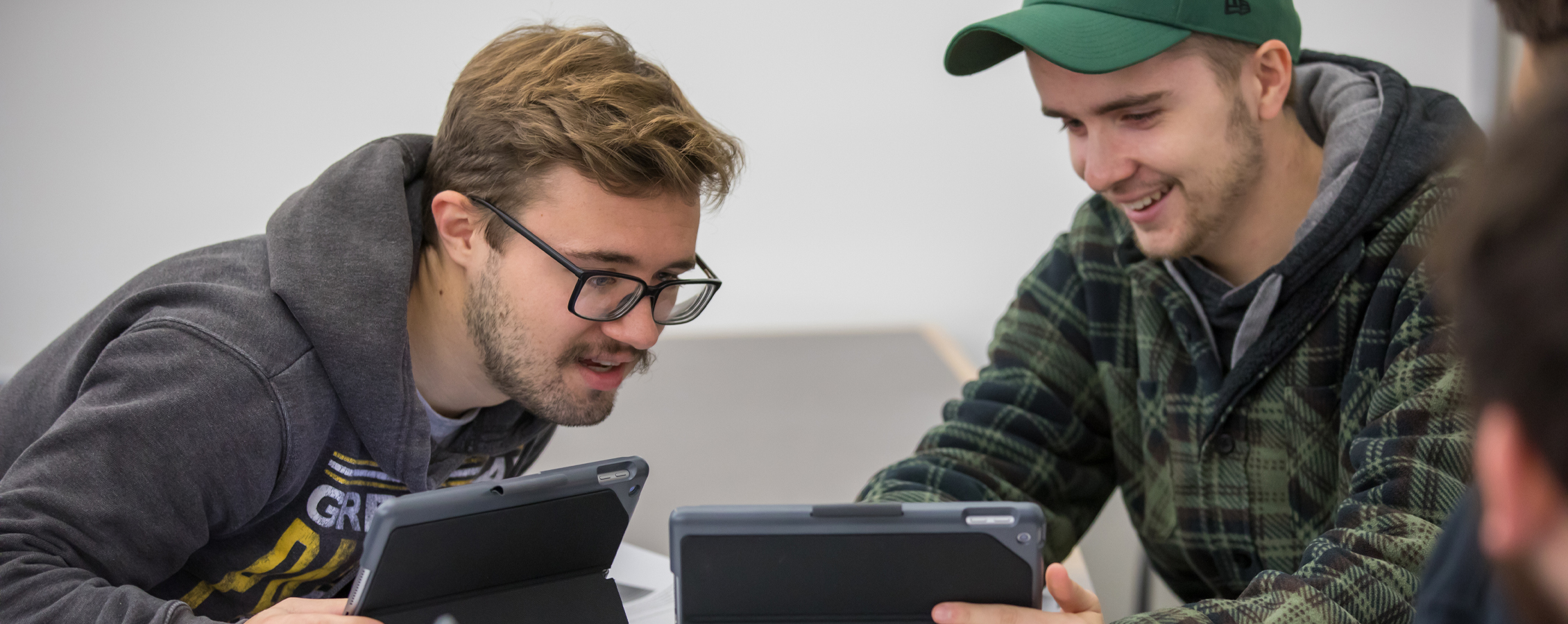 Two smiling students look at tablets together.