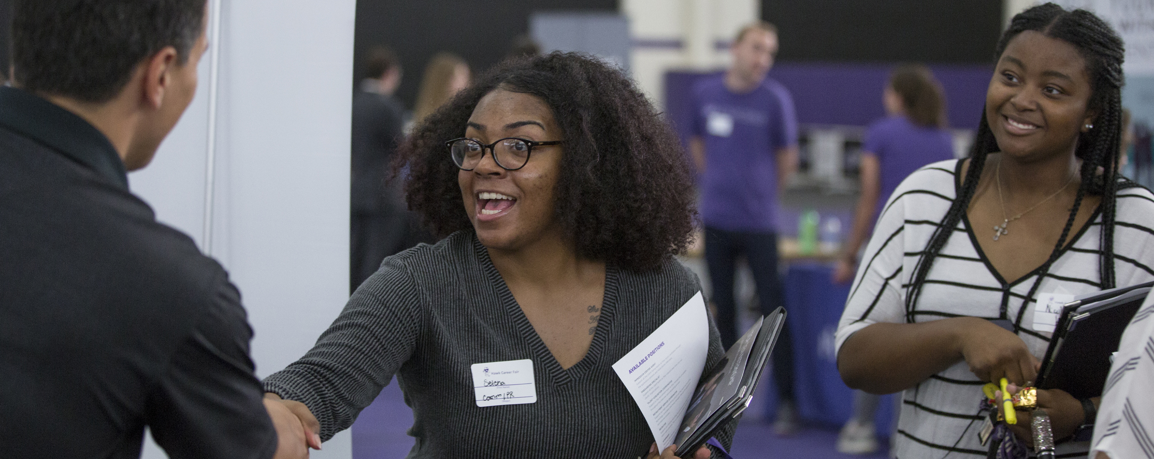 Two people shake hands at a career fair.