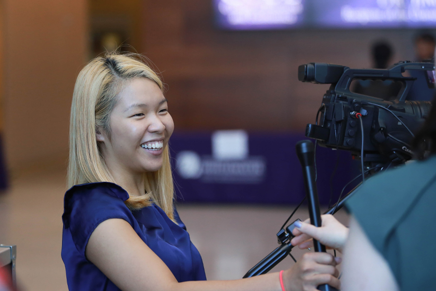 A student stands next to a video camera, smiling.