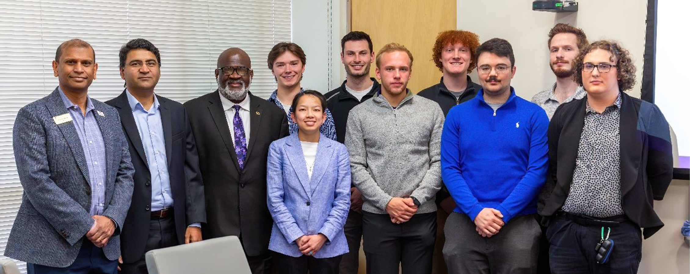 A group of 11 people stand together in a classroom and pose for a photo.