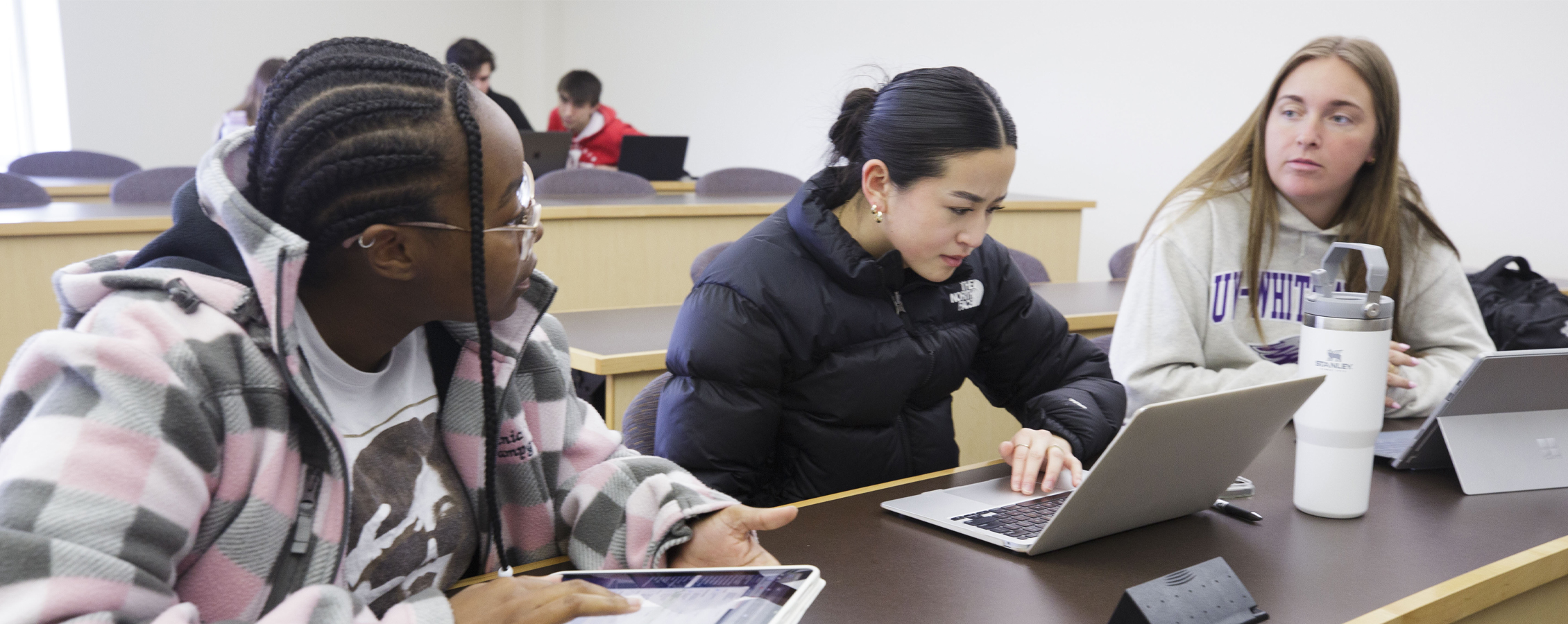 Three students work together at a long table in a classroom.