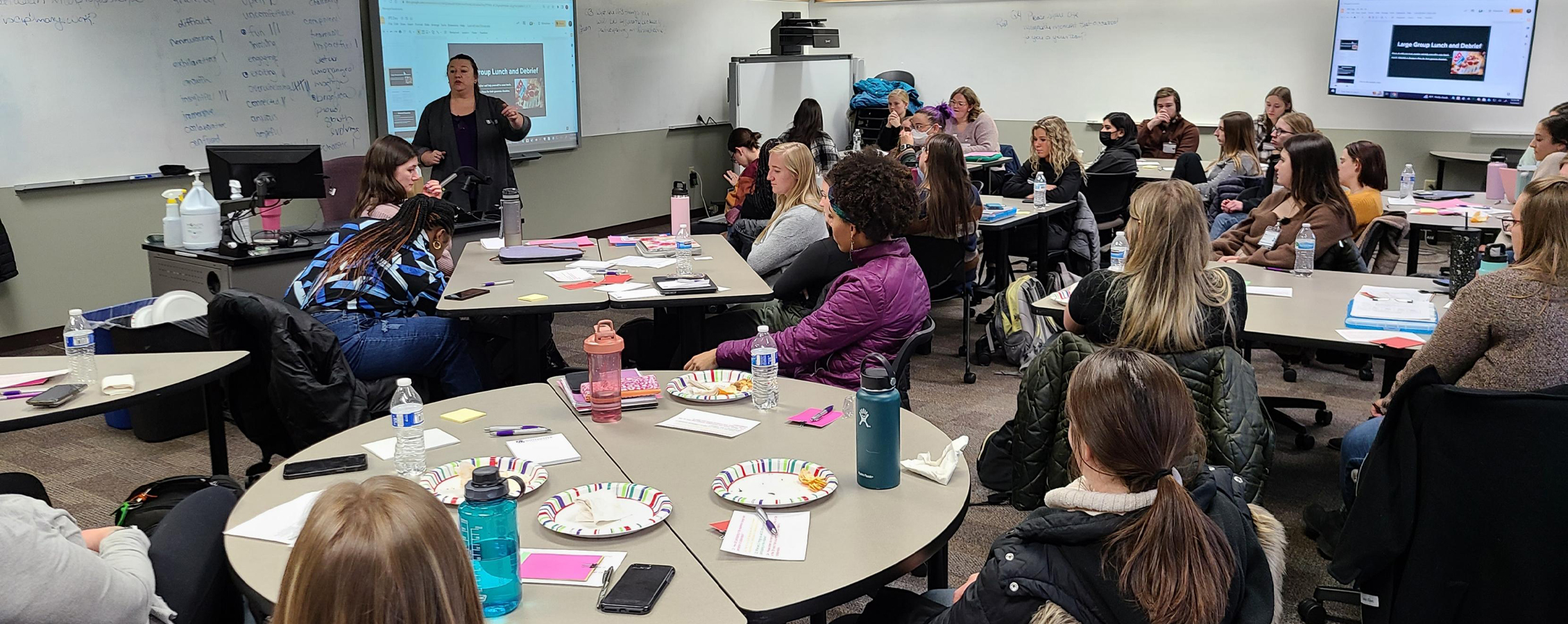 A faculty member speaks to a large group of students in a classroom setting.