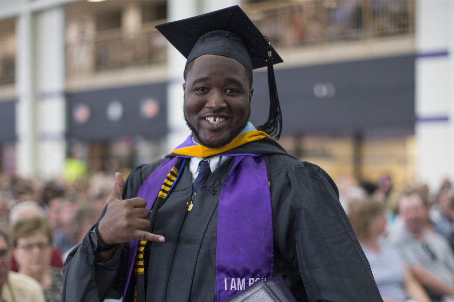 A person wearing their cap and gown at graduation smiles at the camera.