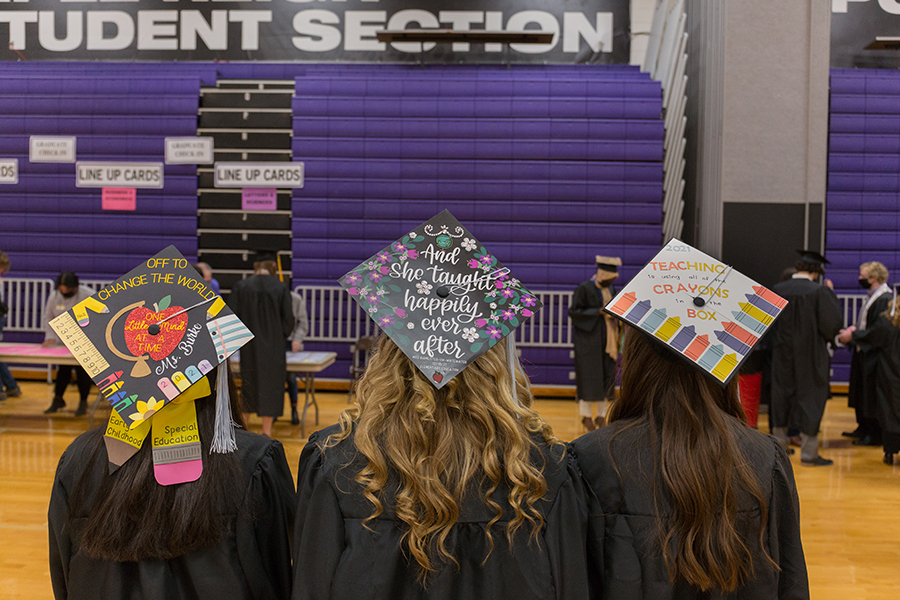 Three education majors show their decorated caps at graduation.