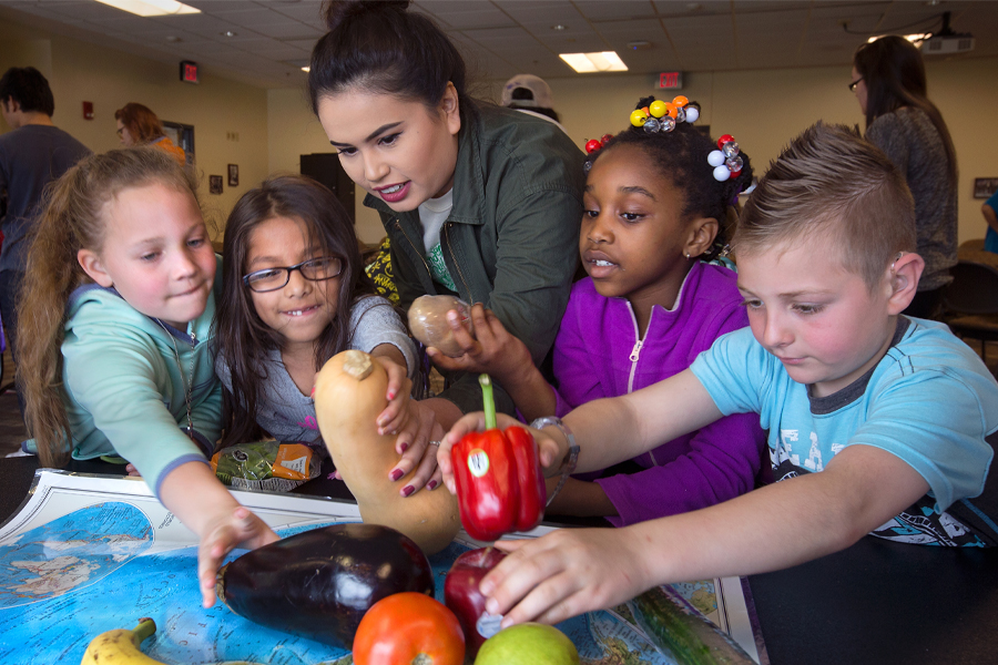 Young students and their teacher place colorful vegetables on a map.