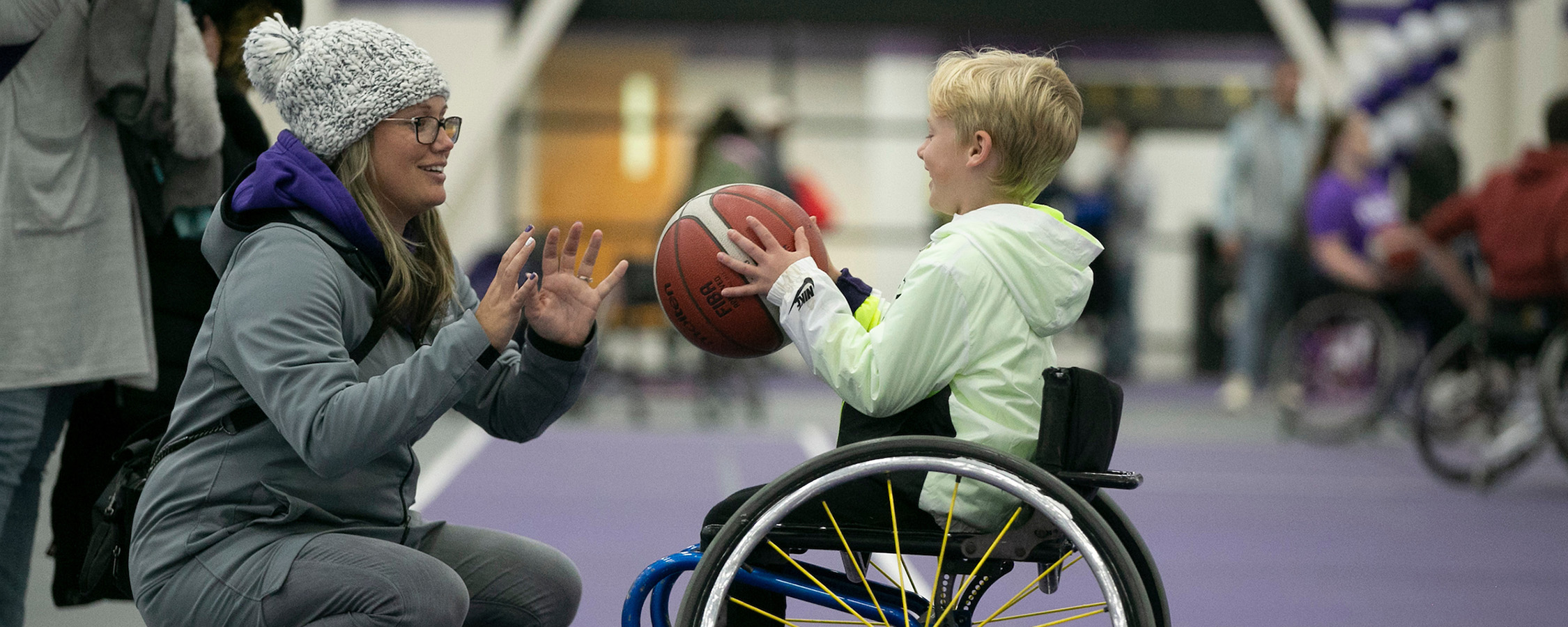 Boy in a wheelchair passing a basketball to a woman crouching in front of him