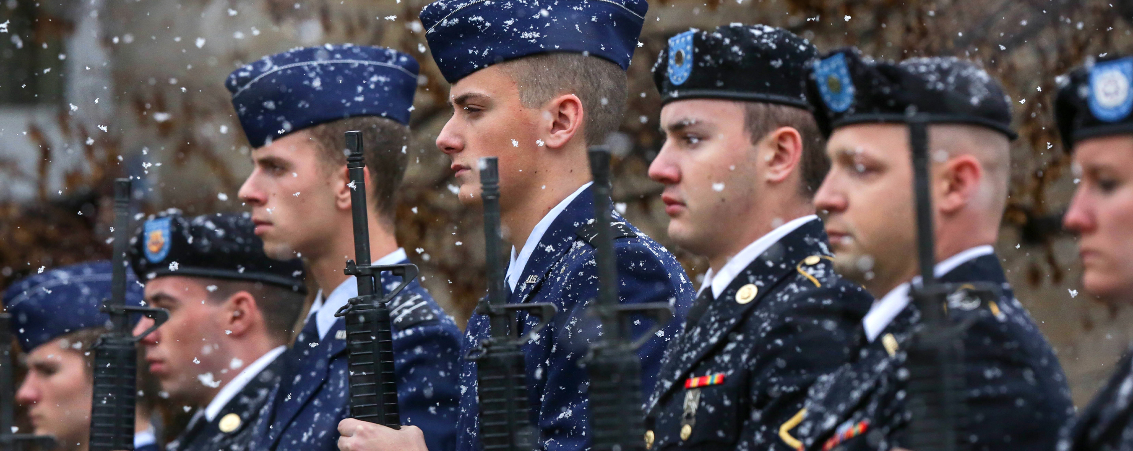 Veterans stand with their rifles as it snows.