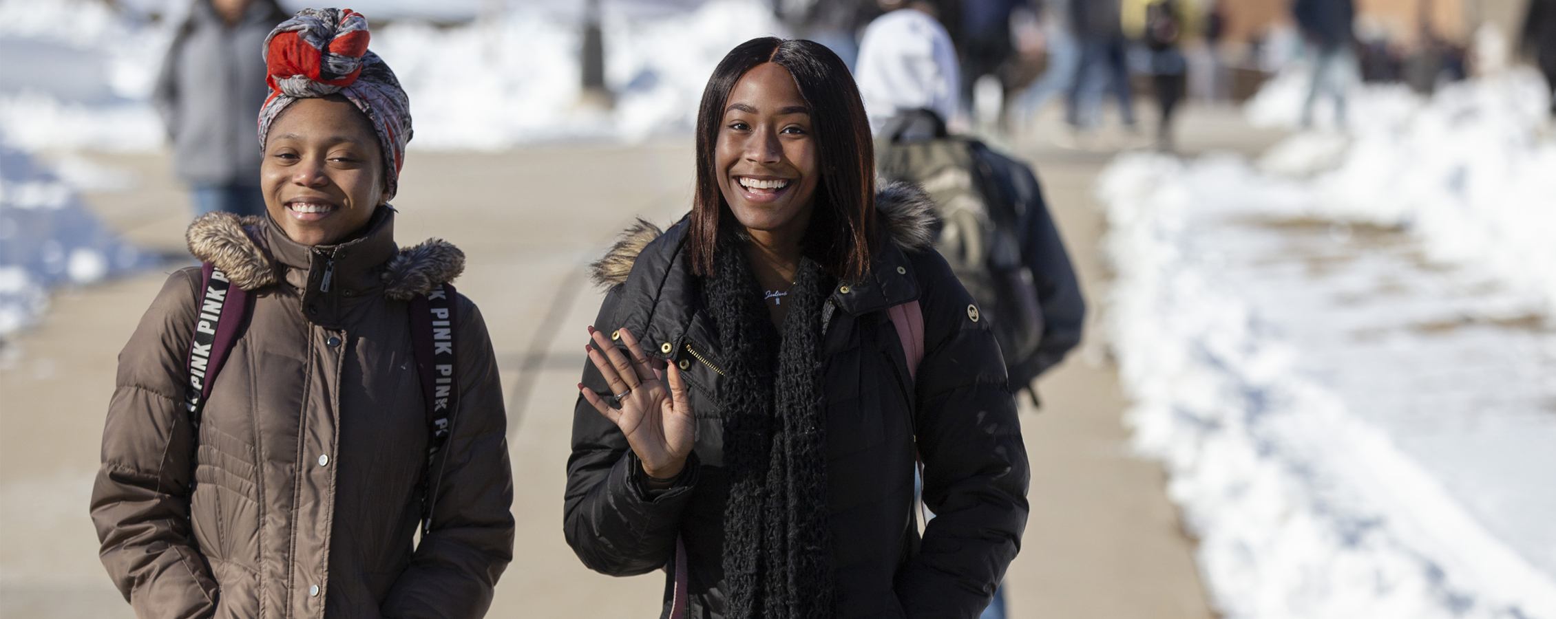 Two students walk outside wearing winter jackets and smile at the camera.