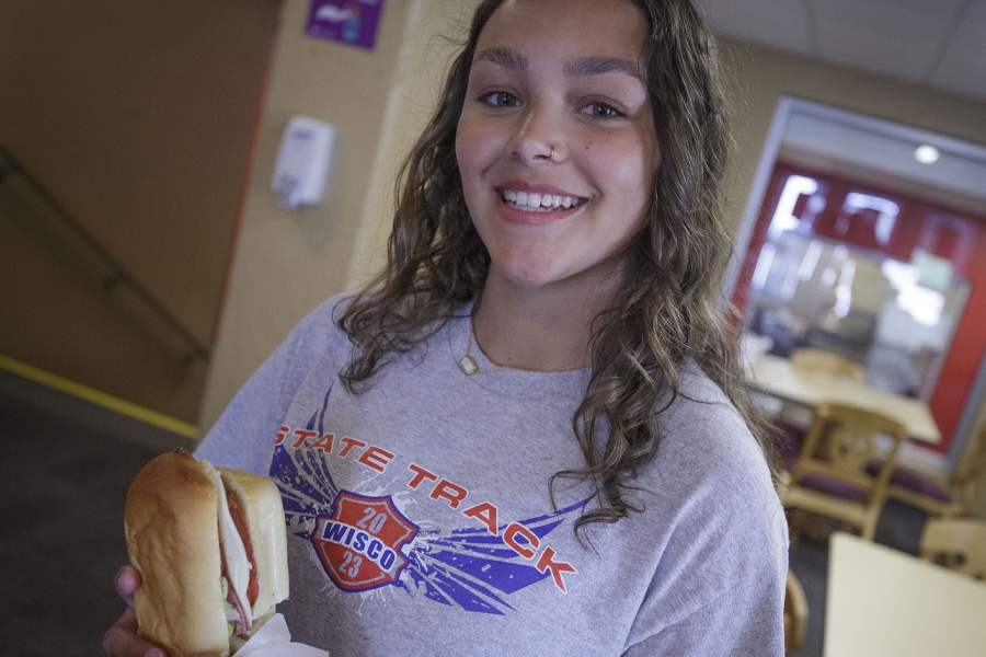 A student smiles while holding a sandwich.