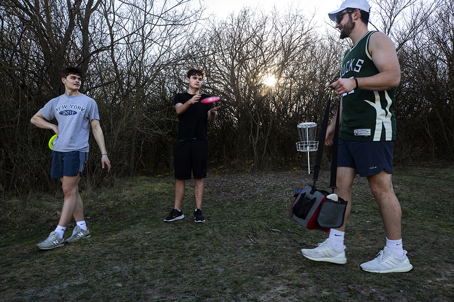 A group of students play frisbee golf during sunset.