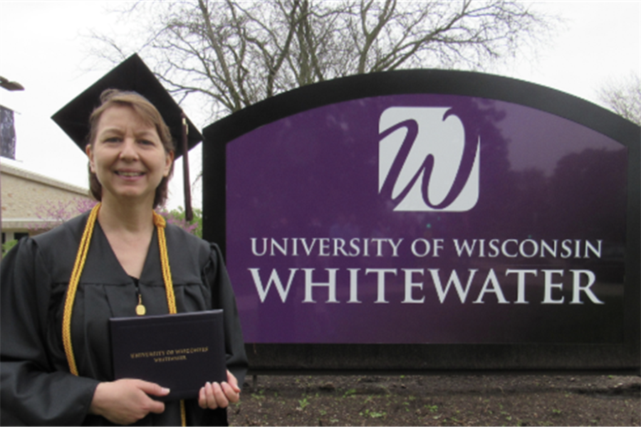 Roseann Stricker holding diploma in front of UW-Whitewater sign