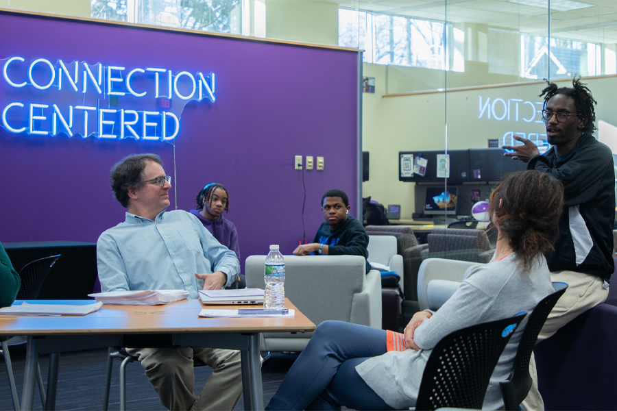 People sit at tables with a purple wall in the background and neon letters that say Connection Centered.