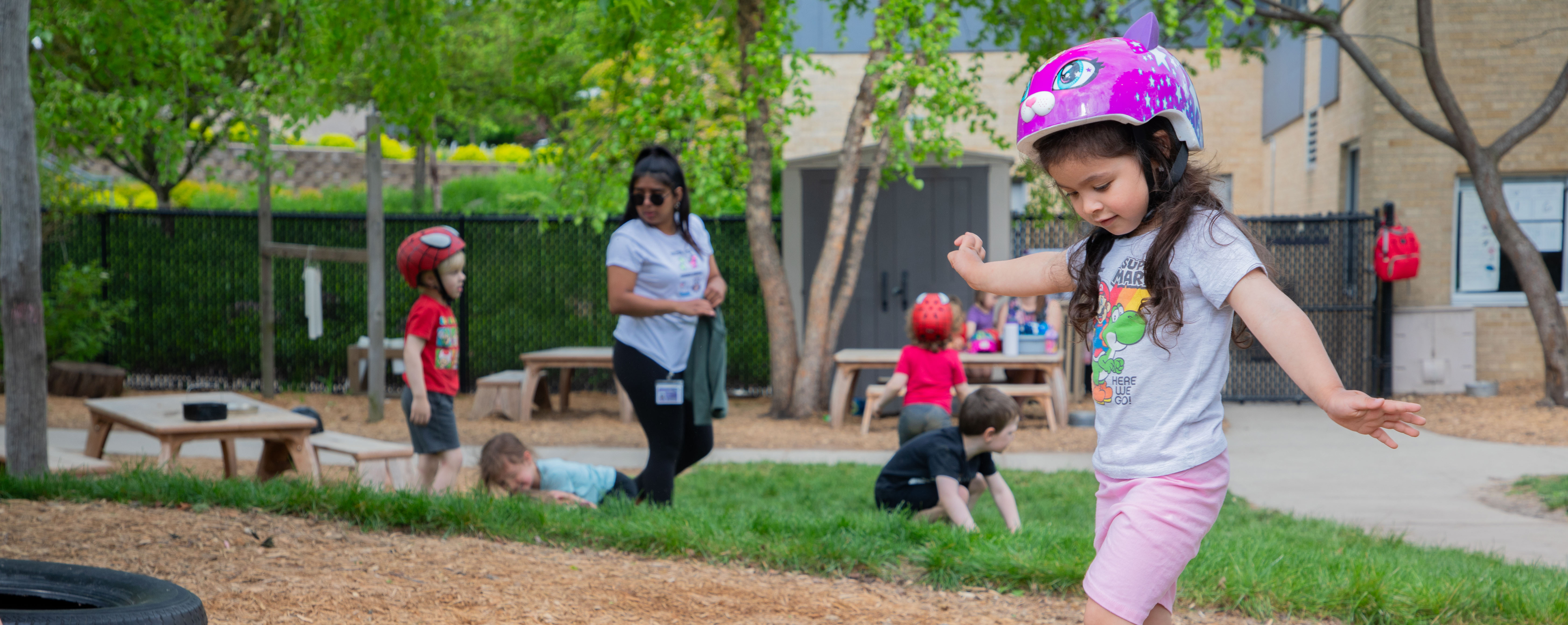 Image of a girl wearing a pink bicycle helmet with other children playing in the background