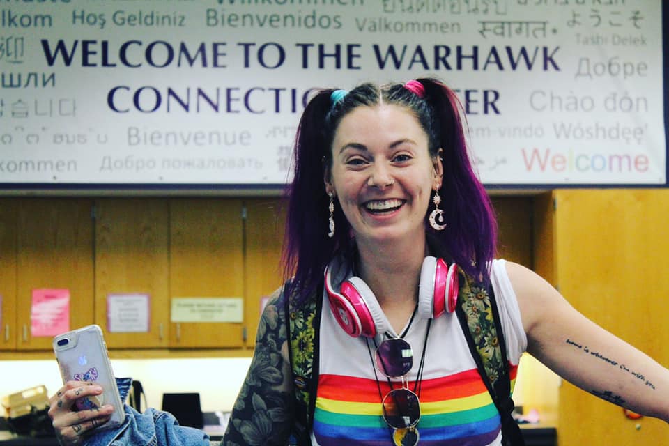 Student smiling in front of the Warhawk Connection Center banner on National Coming Out Day. 