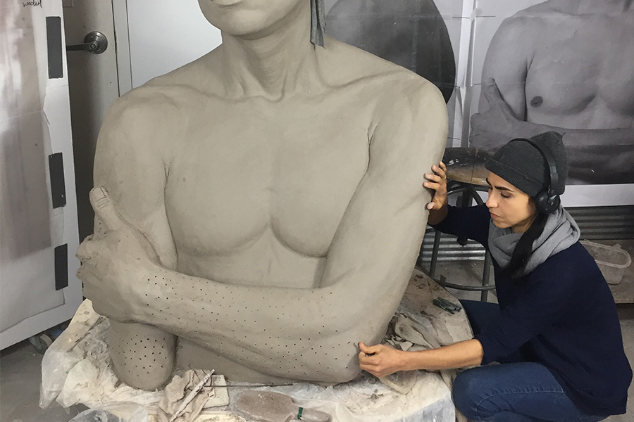 Artist Cristina Córdova sculpting large clay model of human torso.