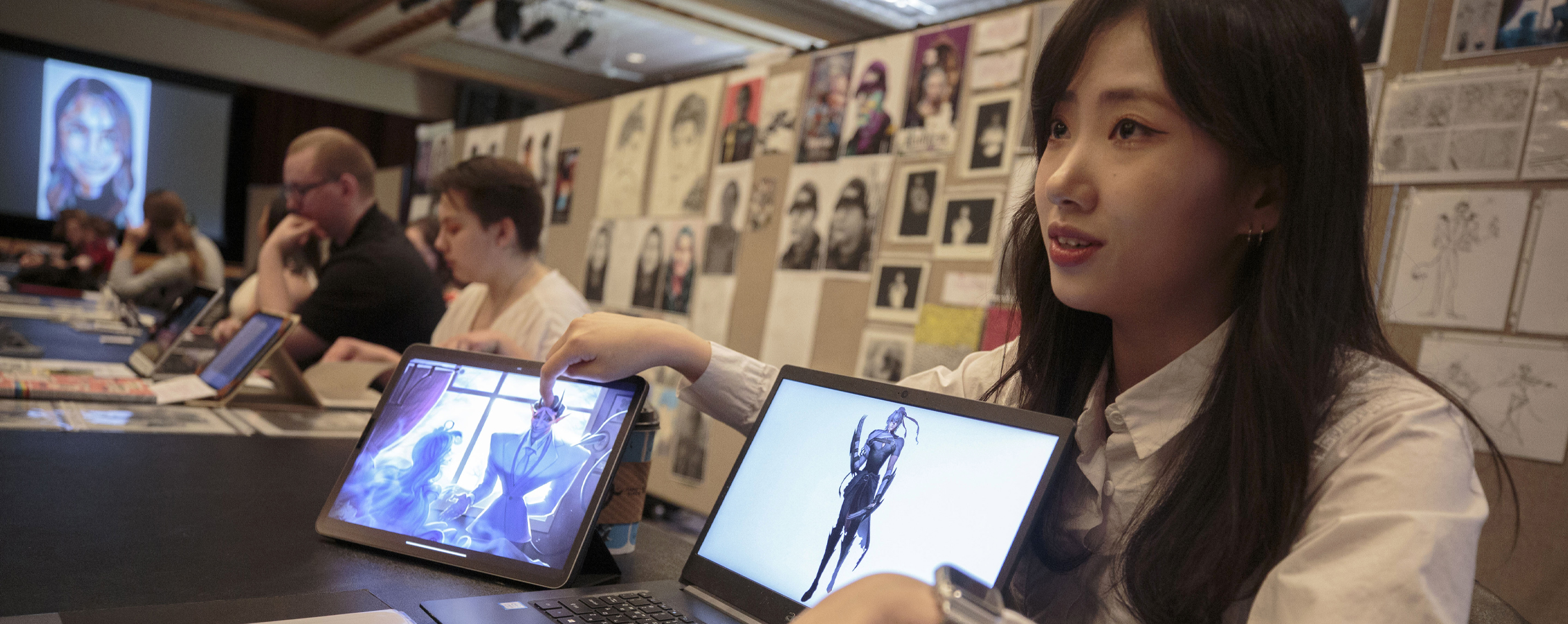 A student sits at a table with two devices that show media arts that they've built.