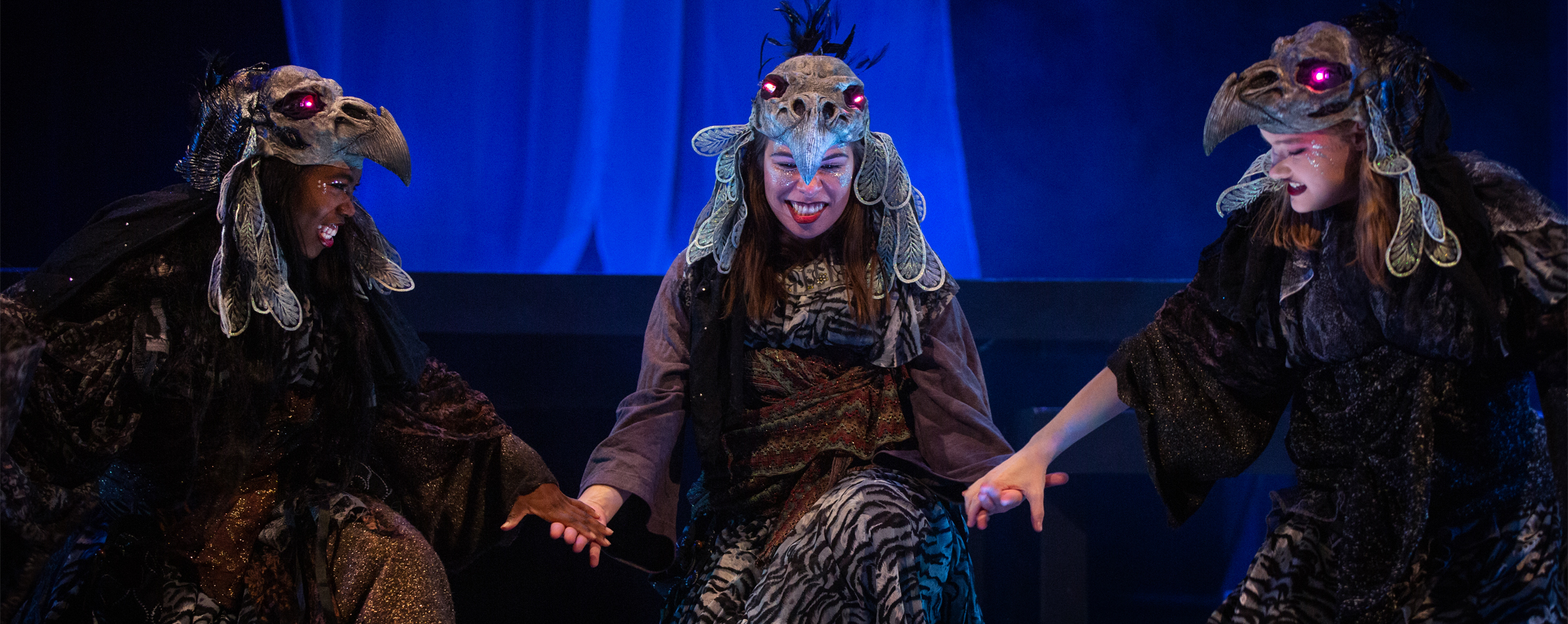 Three students in costume perform on stage.