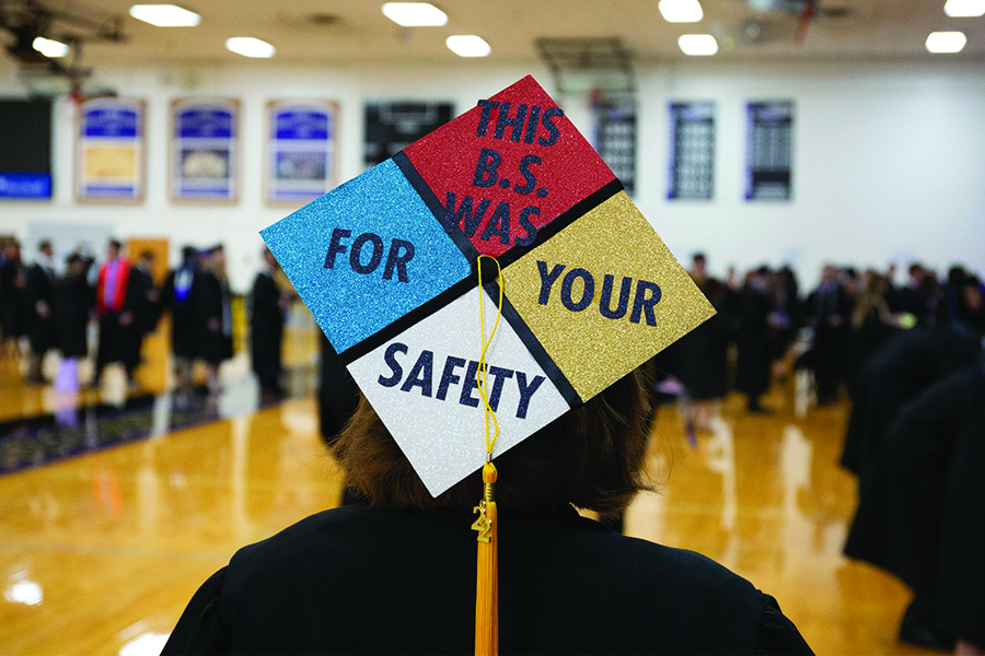 Student at graduation with text that reads "This B.S. was for your safety" printed on the back of their cap.