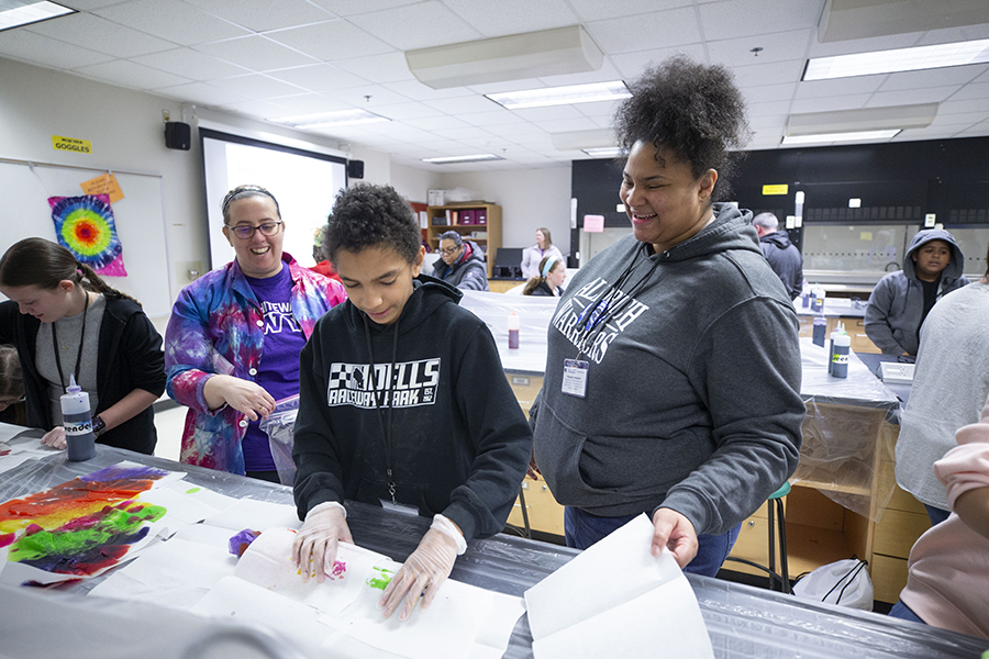 Two adults work in a lab classroom with a young student who is learning about tye dye paints.