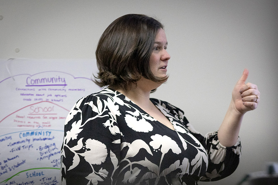 A faculty member in a black and white shirt stands in front of a whiteboard.