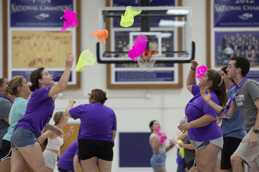 Students face each other in two lines and toss colorful objects back and forth.